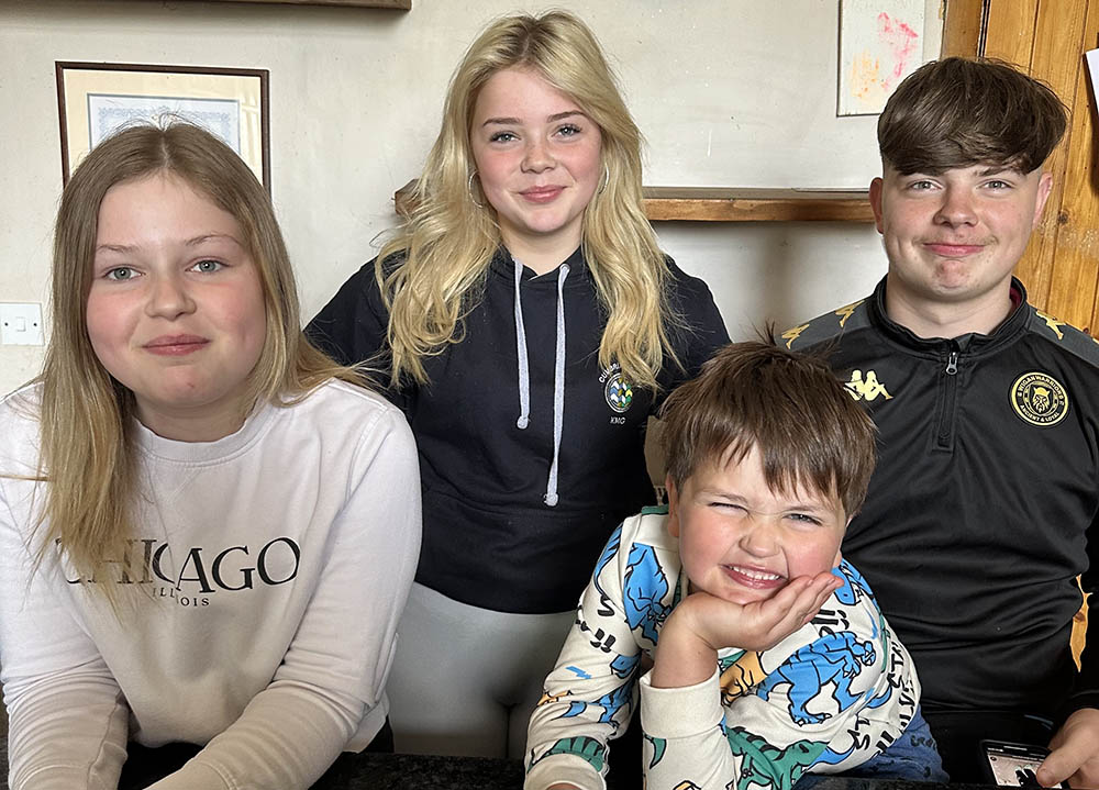 Four children together, smiling for a family photo.