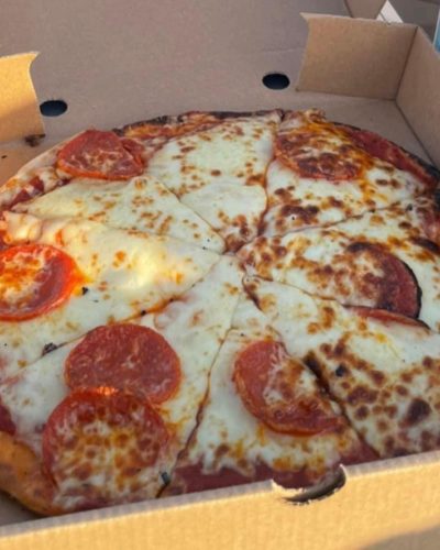 Pepperoni pizza in an open cardboard takeaway box, sliced and topped with melted cheese.